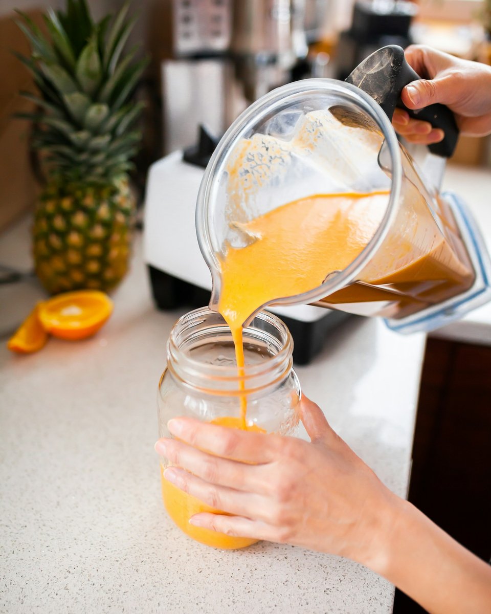 Smoothie orange versé d'un bol de blender dans un bocal en verre