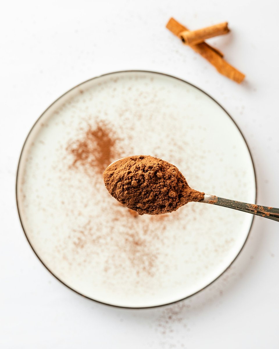 Cuillère de cacao en poudre au-dessus d'un bol de lait, bâtons de cannelle