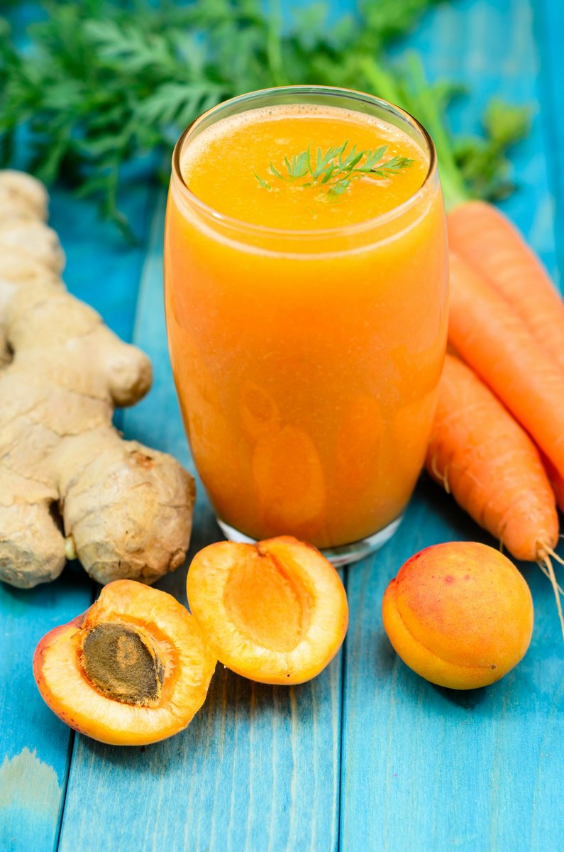 Verre de jus orange entouré de carottes, de gingembre et d'abricots
