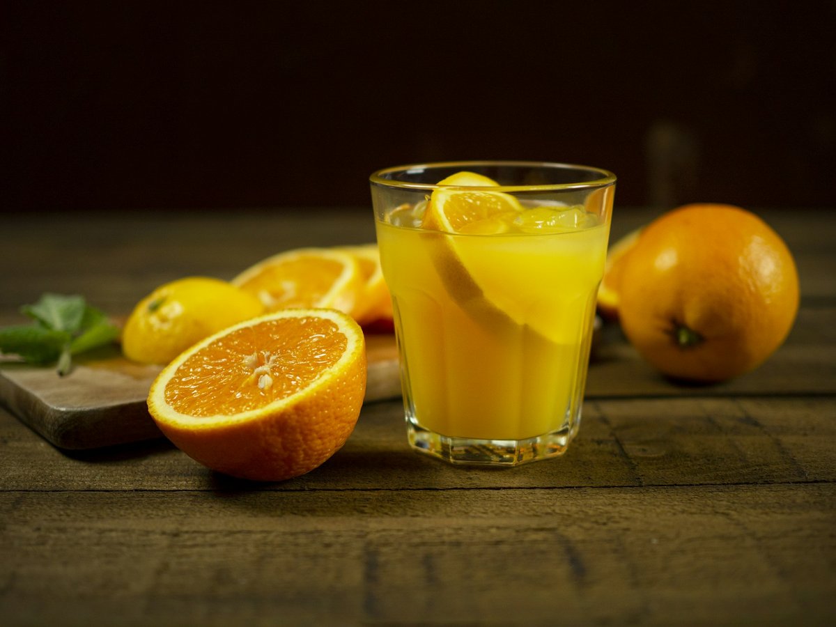 Verre de jus d'orange et oranges coupées sur une planche en bois