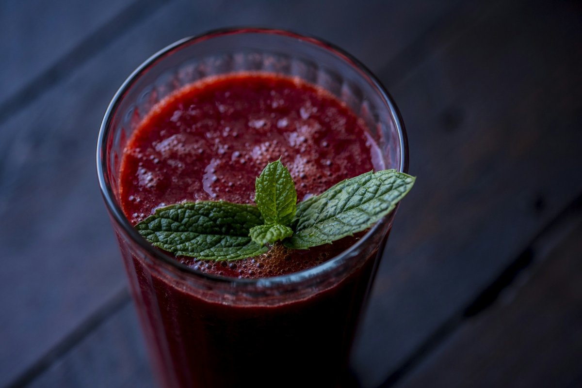Verre de jus rouge sombre garni de menthe sur un fond bleu nuit