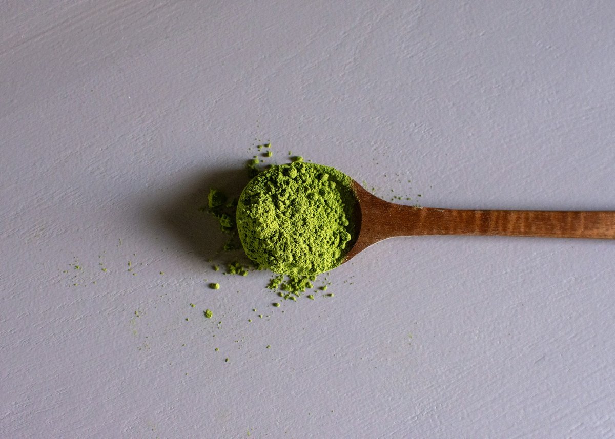 Cuillère en bois remplie de poudre de matcha sur un fond gris clair