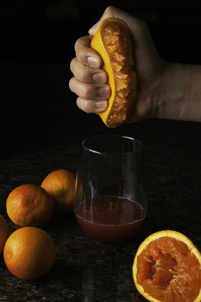 Main pressant une demi-orange sanguine au-dessus d'un verre