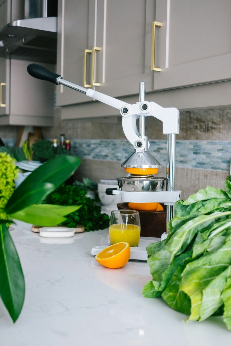 Presse-agrumes à levier sur un plan de travail avec un verre de jus et des feuilles de blettes